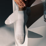 A person wearing white ankle socks with a subtle textured pattern and the brand name 'Dr. Scholl's' printed on the toes, posed on a white geometric surface with dramatic shadows. thumbnail