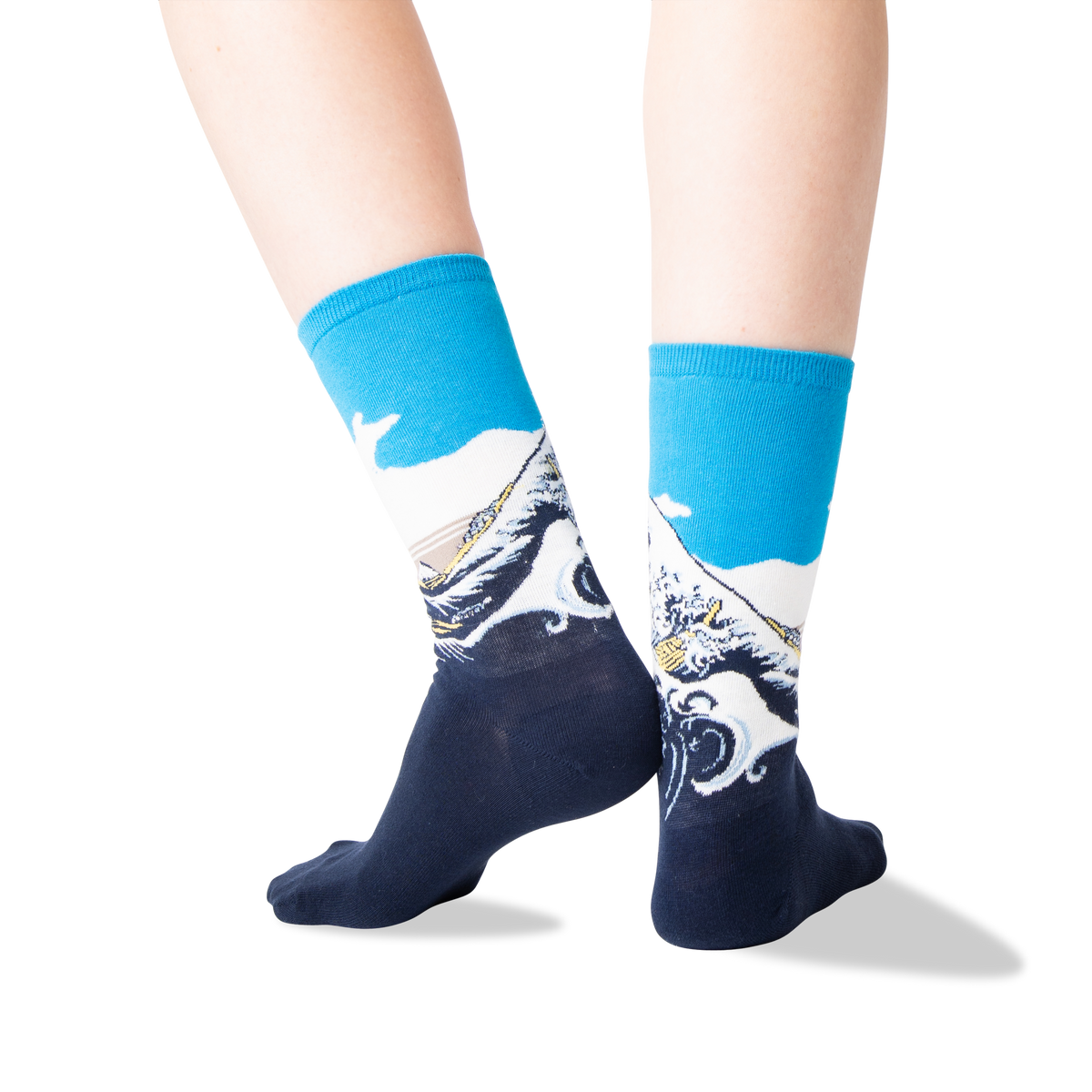 A pair of crew socks worn on a person's feet, featuring a blue and white wave design inspired by Hokusai's 'Great Wave' style print, shown against a plain white background.