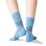 A pair of crew socks worn on feet, featuring an abstract landscape-like print in shades of light blue, teal, and lavender-gray with white and gray brushstroke details. The background is a clean white studio backdrop.