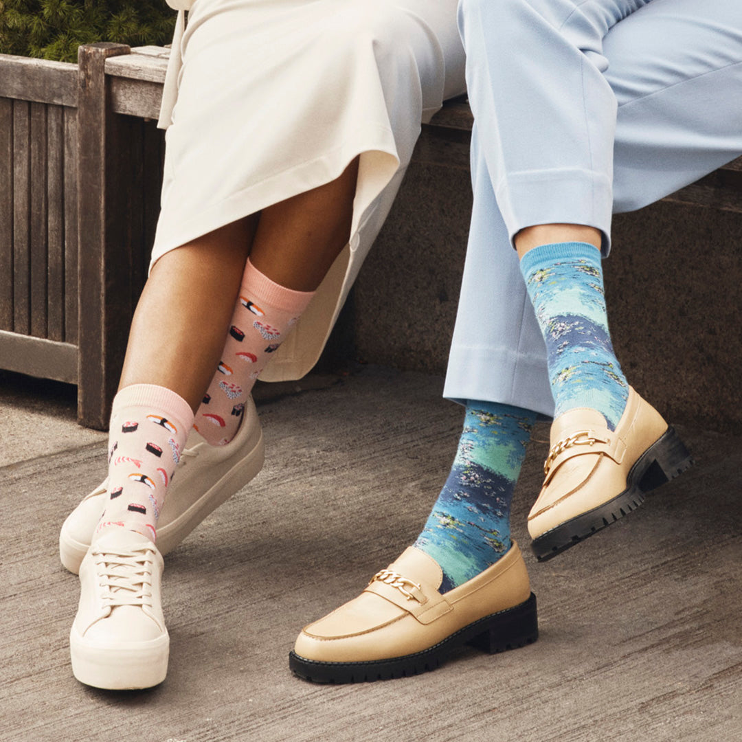 Two women sitting on a bench wearing HOTSOX novelty socks.