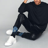 Person wearing black outfit with blue patterned socks sitting on a gray floor. thumbnail