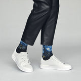 Person wearing black leather pants and white sneakers with blue patterned socks on a gray background thumbnail