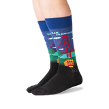A pair of crew socks worn on a person's feet, featuring a colorful graphic of the Golden Gate Bridge and a trolley train in San Francisco on a blue background, with a black toe and heel section. thumbnail