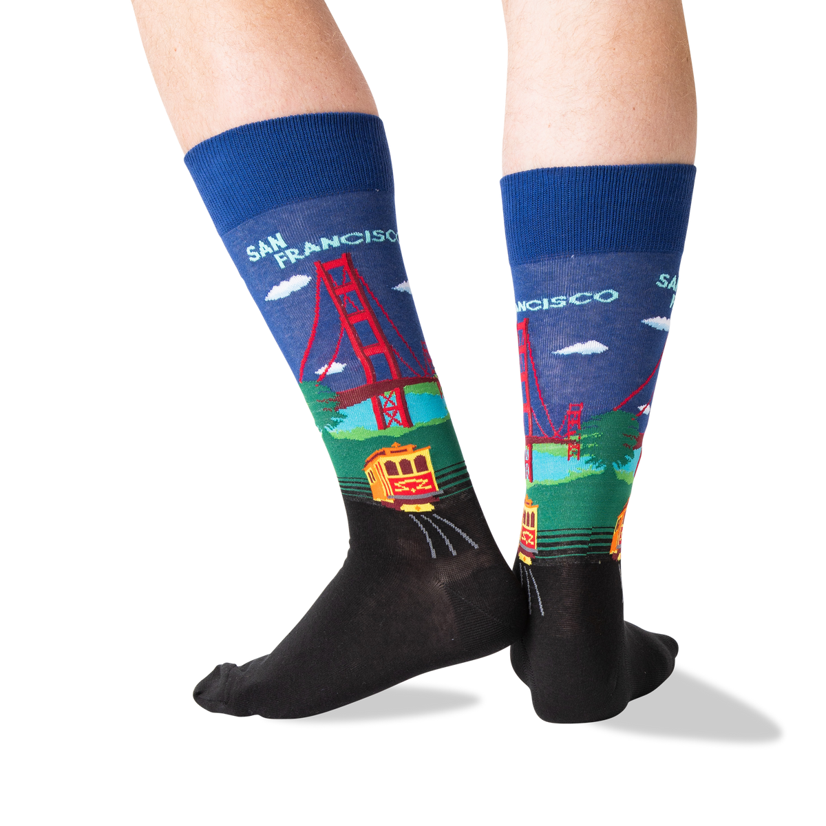 A pair of crew socks worn on feet, featuring a colorful San Francisco-themed graphic with the Golden Gate Bridge, trolleybus, and 'SAN FRANCISCO' text on a white background.