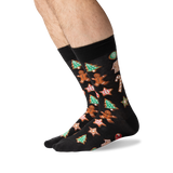 A pair of black crew socks with a festive Christmas gingerbread pattern, worn on a person's feet against a clean white background.