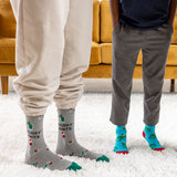 Two people wearing festive socks with holiday-themed designs on a carpeted floor.