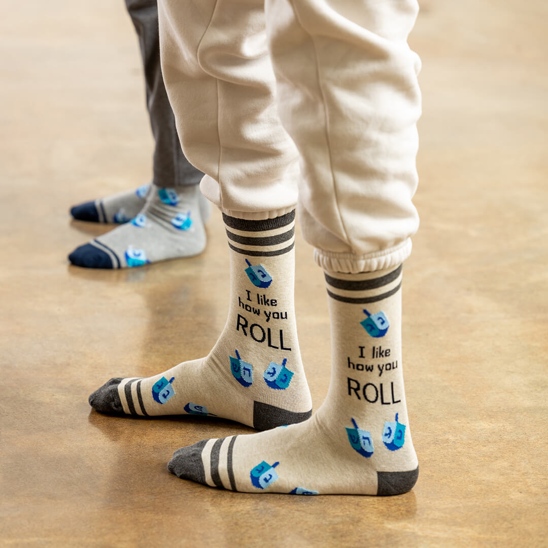 Beige socks with text and blue dreidel design worn by a person on a wooden floor.