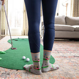Person playing mini golf indoors with a green mat and golf ball on a patterned rug. thumbnail