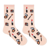A pair of light pink crew socks with a repeating pattern of various makeup items, including lipstick, eyeshadow palettes, brushes, and compacts, displayed on a clean white background.