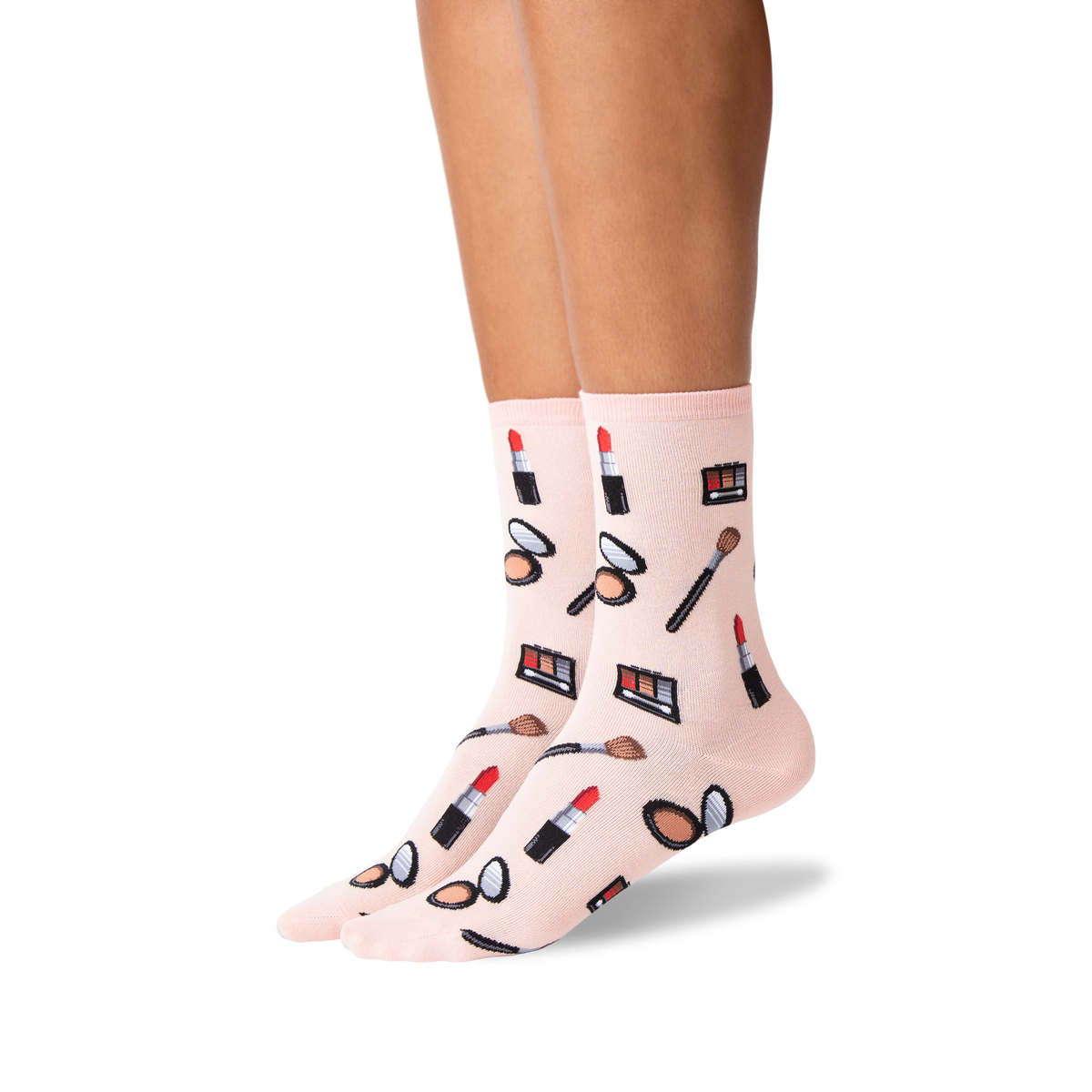 A pair of light pink crew socks with a colorful makeup-themed print of lipsticks, eyeshadow palettes, brushes, and compact mirrors, shown on a model's feet against a white background.