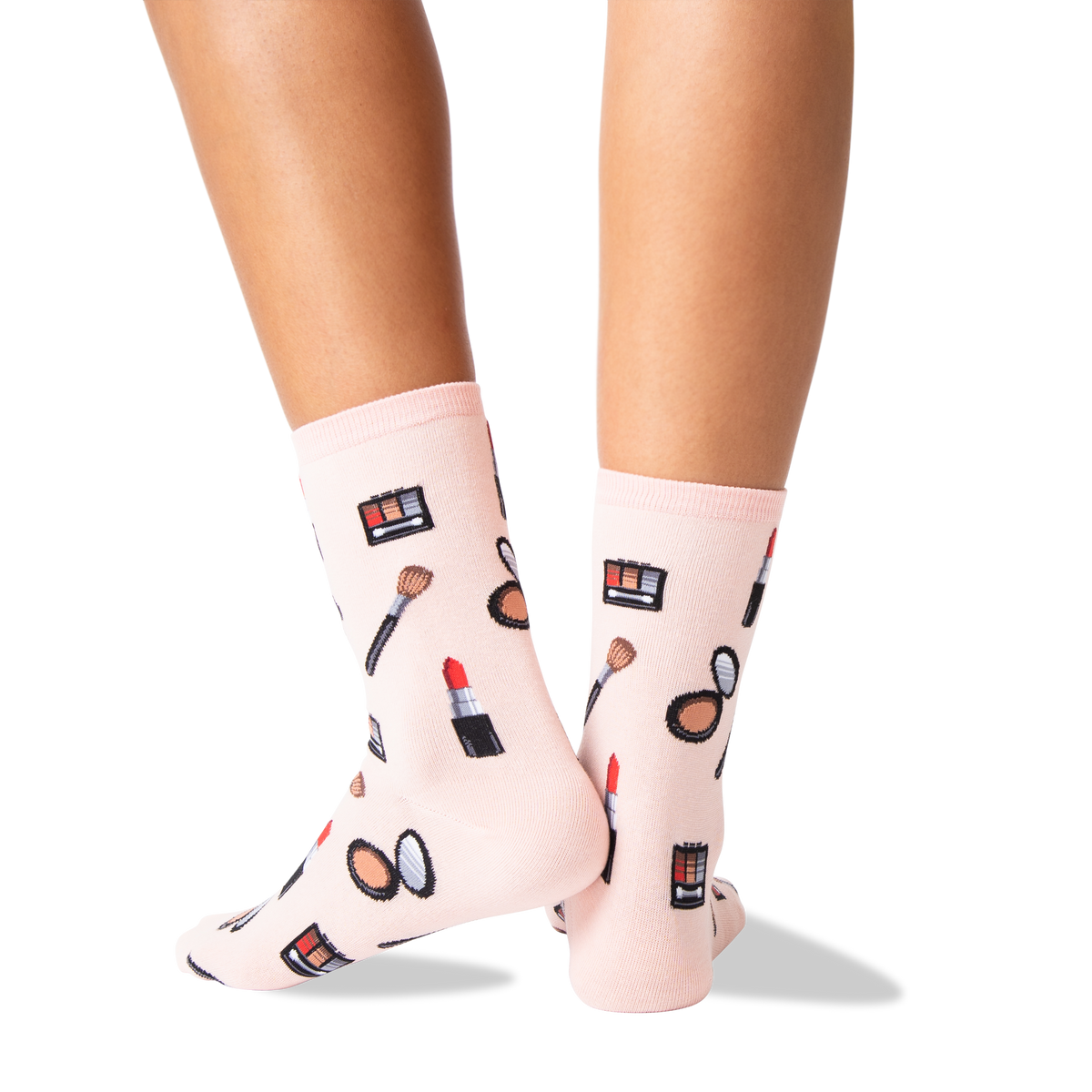 A pair of light pink crew socks with a makeup-themed print, worn on a person's feet against a clean white background.