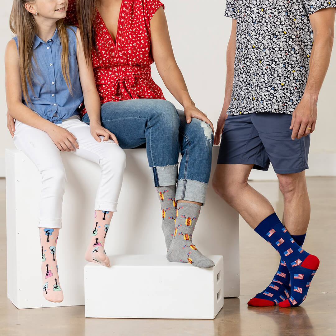 Three people sitting on a white block, wearing colorful patterned socks.