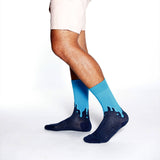 A person's legs wearing crew socks with a dark navy blue base and a bright blue dripping design along the top, shown against a plain white studio background.