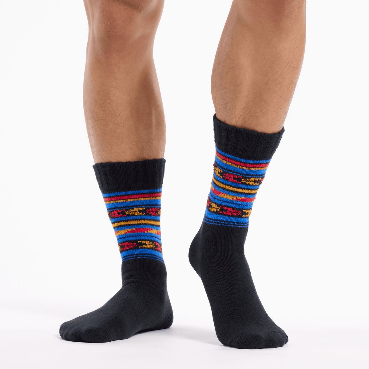 A pair of crew socks worn on a person's feet, featuring a black base with a vibrant multicolor striped pattern in red, blue, yellow, and orange around the calf.