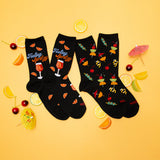 Two pairs of black socks with colorful designs on a yellow background with lemon slices and cocktail umbrellas.