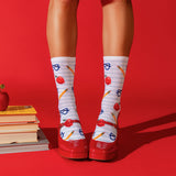 White knee-high socks with a striped pattern and school-themed illustrations of red apples, yellow pencils, and blue glasses, worn with red Mary Jane shoes against a solid red background. thumbnail