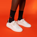 White sneakers worn with black socks featuring a cherry design on an orange background