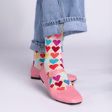 Colorful heart-patterned socks worn with pink shoes and blue jeans on a light gray background thumbnail