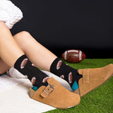 Person wearing black socks with football patterns, sitting on grass with a Wilson football in the background.