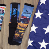 Two pairs of socks with Jeep-themed designs on a wooden surface next to an American flag.