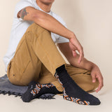 Person wearing black socks with patterned toes and heels, sitting on a beige surface. thumbnail