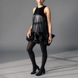 Woman wearing a black dress with ruffled layers and tights on a gray background