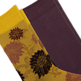 Two folded dress socks shown on a white background. One sock is gold with a dark brown and mauve floral pattern, and the other is solid deep plum purple. thumbnail