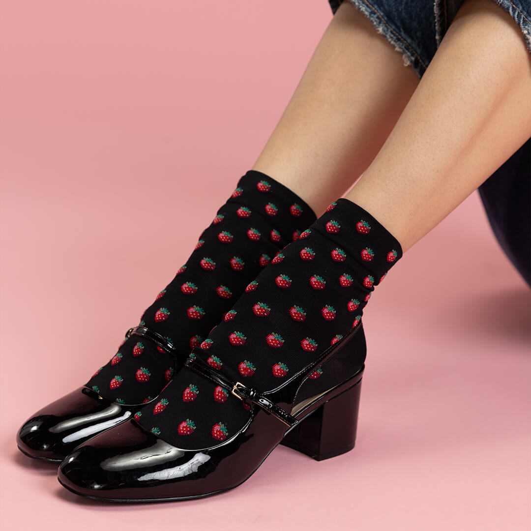 Black shoes with strawberry pattern socks on a pink background