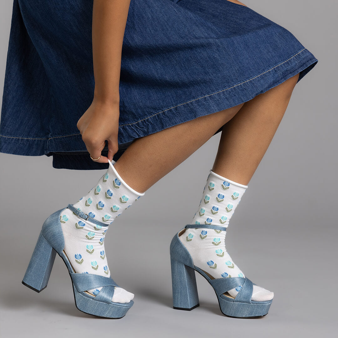 Person wearing denim platform shoes with white socks featuring blue hearts on a gray background