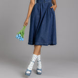 Person wearing a blue denim dress holding blue tulips on a gray background thumbnail