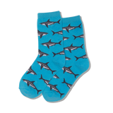 Child wearing blue socks with shark pattern playing Scrabble on a textured surface.