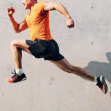 Man in orange shirt and black shorts running in front of a concrete surface thumbnail