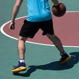 Person holding a basketball on a court wearing a blue shirt, black shorts, and colorful shoes. thumbnail
