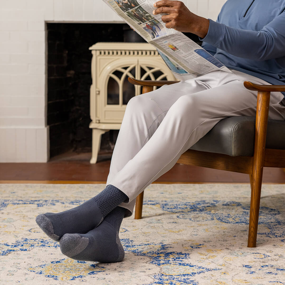 Person sitting in a chair reading a newspaper with a fireplace in the background
