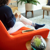 Person sitting on an orange chair in a living room, holding a notebook. thumbnail