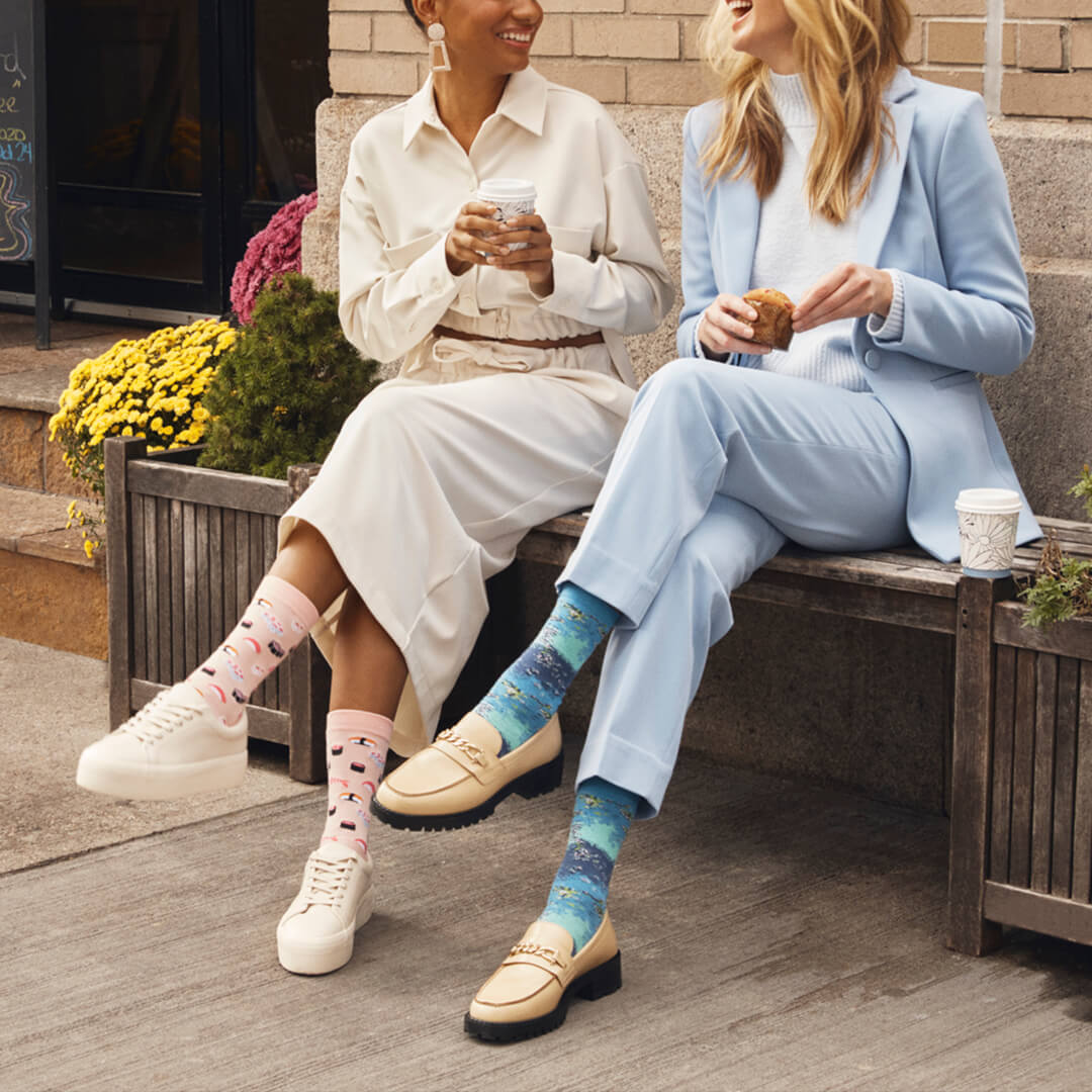 Two women sitting on a bench wearing colorful socks, one with pink polka dots and the other with a starry pattern.