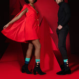 Person wearing a red dress with a cape and another person in black attire on a red background wearing Santa-themed Mona Lisa socks thumbnail