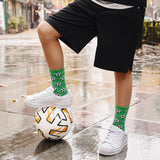 Person balancing on a soccer ball with green socks featuring black patterns, standing on a wet pavement.