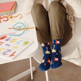 Child wearing blue socks with guitar design sitting on a chair next to a table with colorful letters. thumbnail