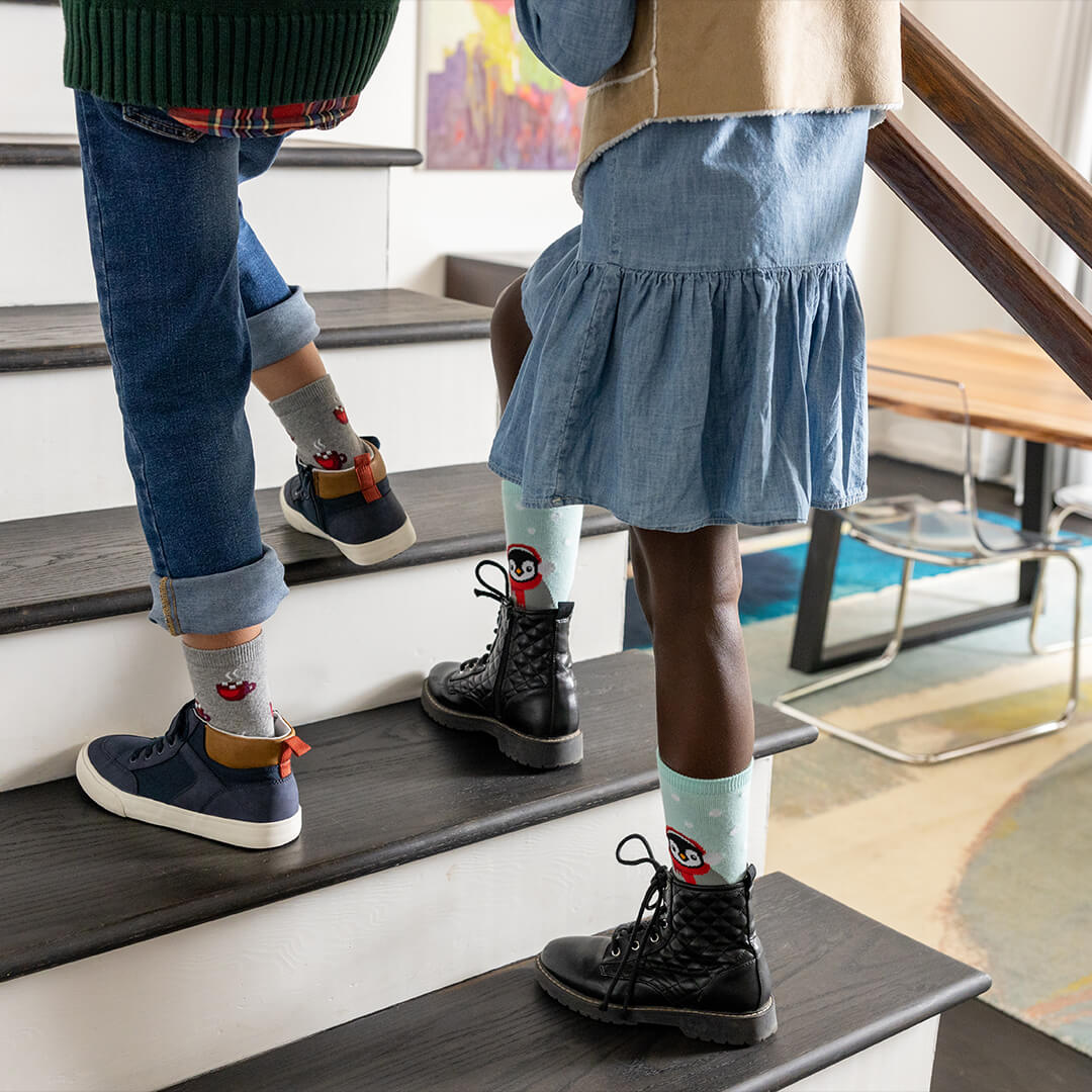 Two children standing on a staircase wearing colorful socks with cartoon characters.