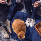 Two people sitting on a couch with a cat, wearing socks with coffee cup designs. thumbnail