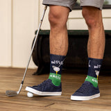 Person wearing socks with a golf theme and holding a golf club on a wooden floor. thumbnail