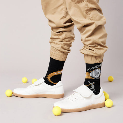 Person wearing black socks with graphic designs, beige pants, and white sneakers on a light gray background.