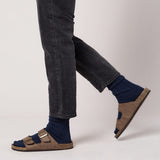 Brown sandals worn with dark jeans and navy socks on a light gray background