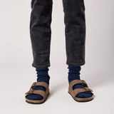 Person wearing blue socks, dark jeans, and brown sandals on a white background thumbnail
