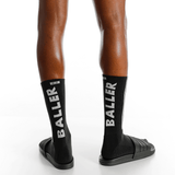 Black socks with 'BALLER' branding worn by a person on a white background