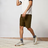 Person wearing olive green shorts and white sneakers on a neutral background thumbnail