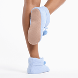 Light blue slippers with pom-poms worn by a person on a white background