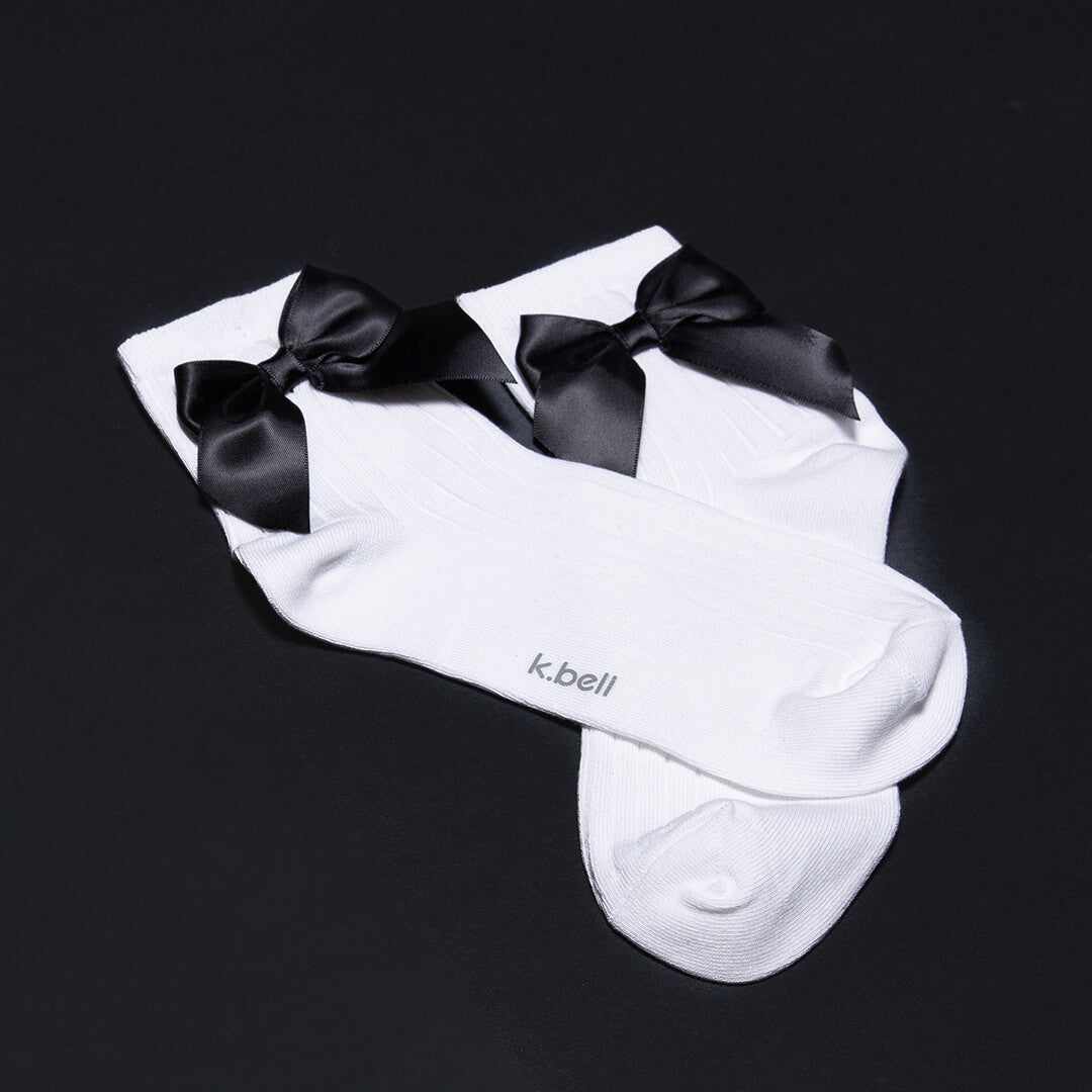 White socks with black bows on a black background, featuring the brand 'k.bell'.