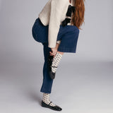 Person wearing blue jeans, a beige sweater, and patterned bow socks on a plain background